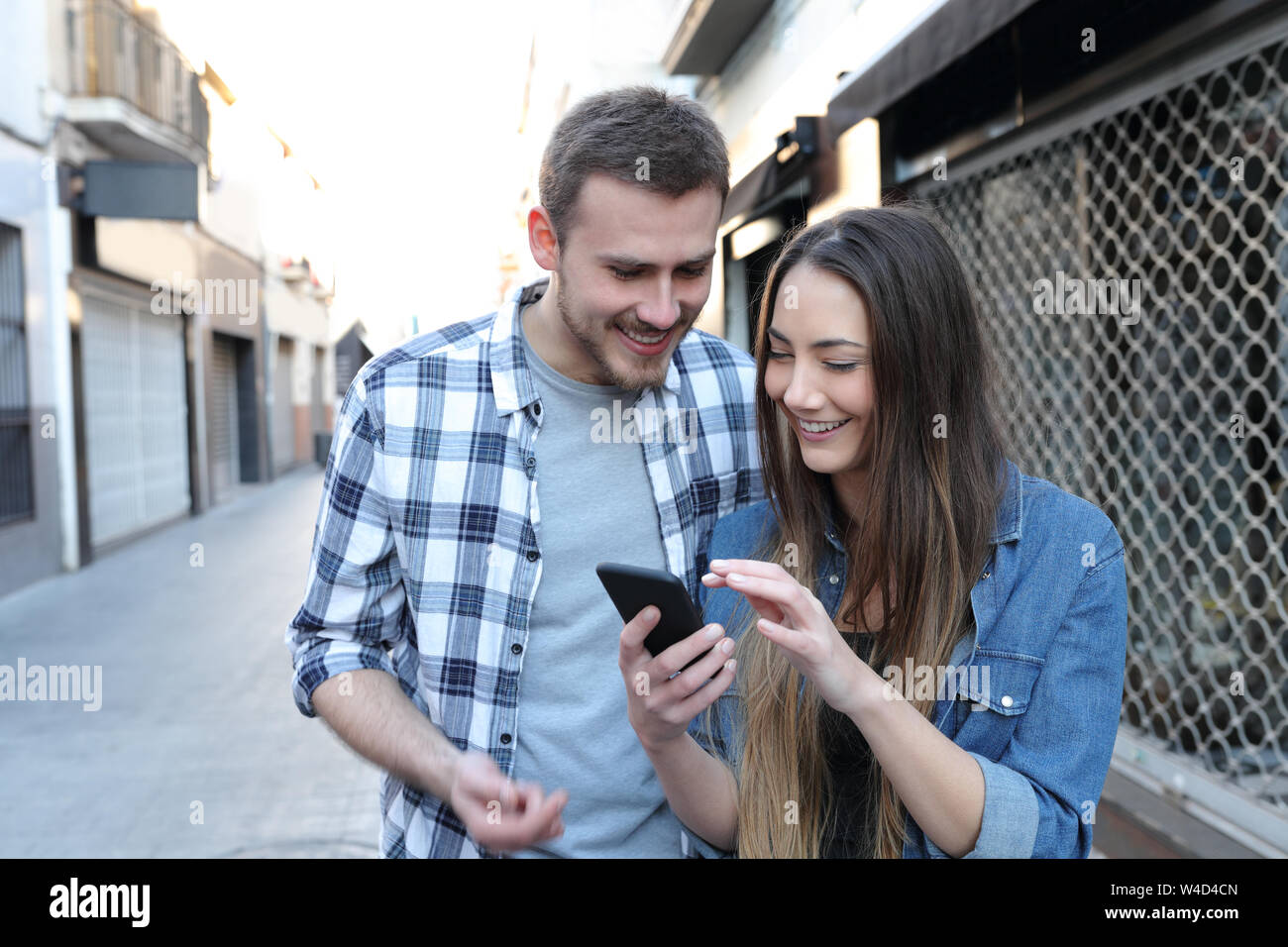 Felice coppia controllo smart phone contenuto insieme a piedi in strada Foto Stock