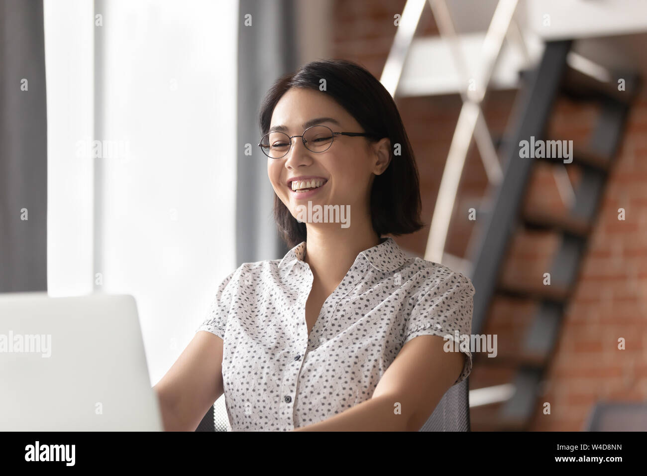 Allegro asian imprenditrice di ridere guardando laptop seduto alla scrivania Foto Stock