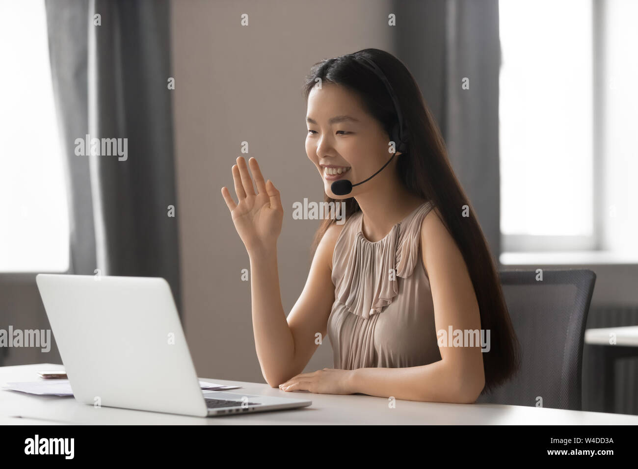 Sorridente asian imprenditrice di indossare un auricolare wireless sventolando fare chat video Foto Stock