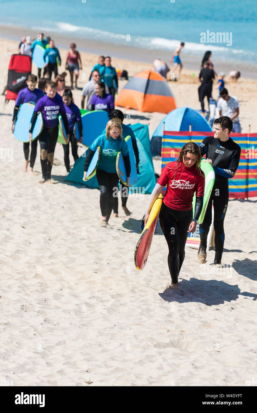 Un istruttore di surf da Fistral Beach Surf School portando la sua classe di studenti attraverso Fistral Beach dopo una lezione di surf. Foto Stock