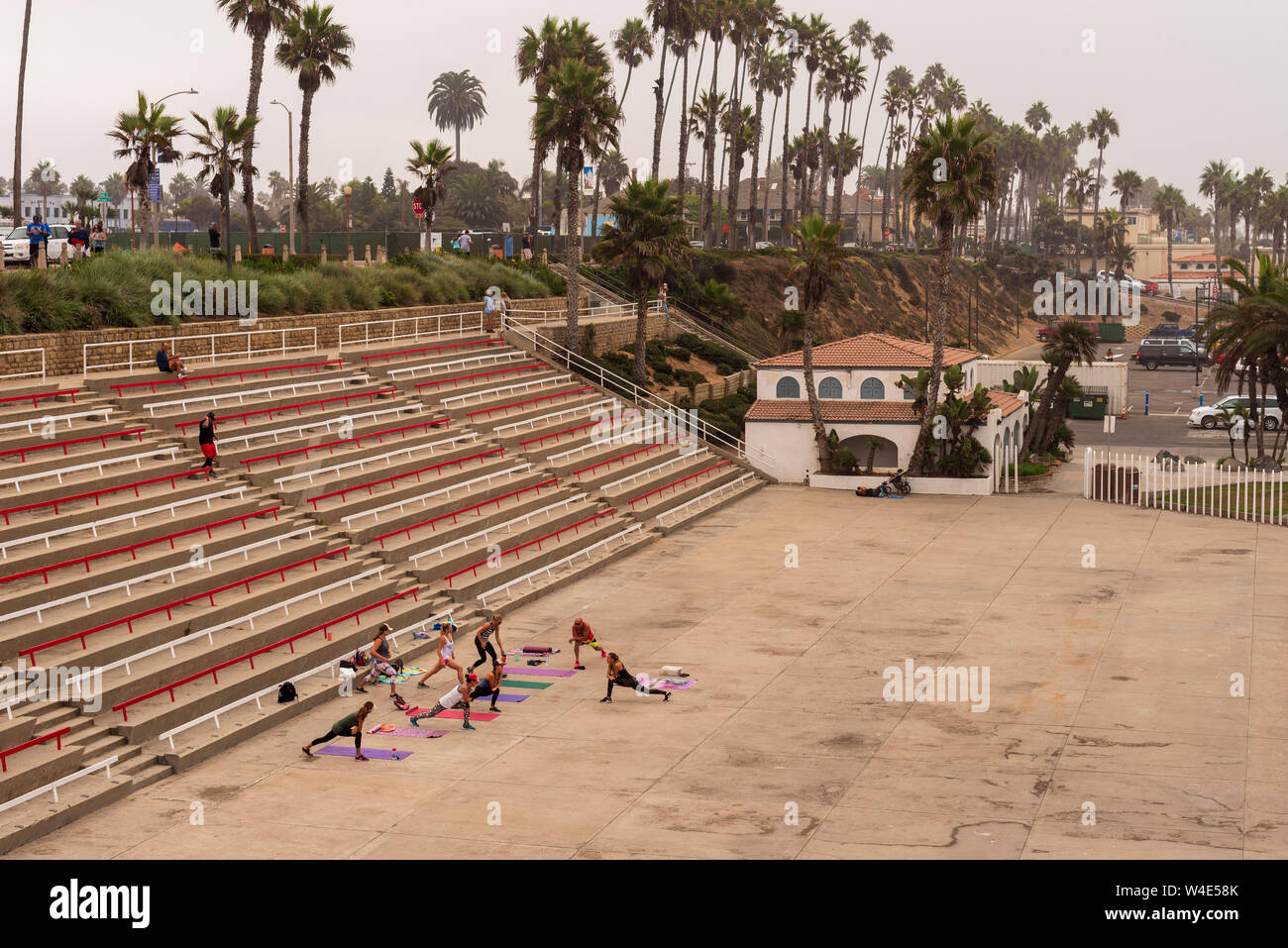 Un gruppo di persone con stuoie di allenamento sul concerto sotto le gradinate sono di esercizio. Oltre al mattino in ghisa e palme. Foto Stock