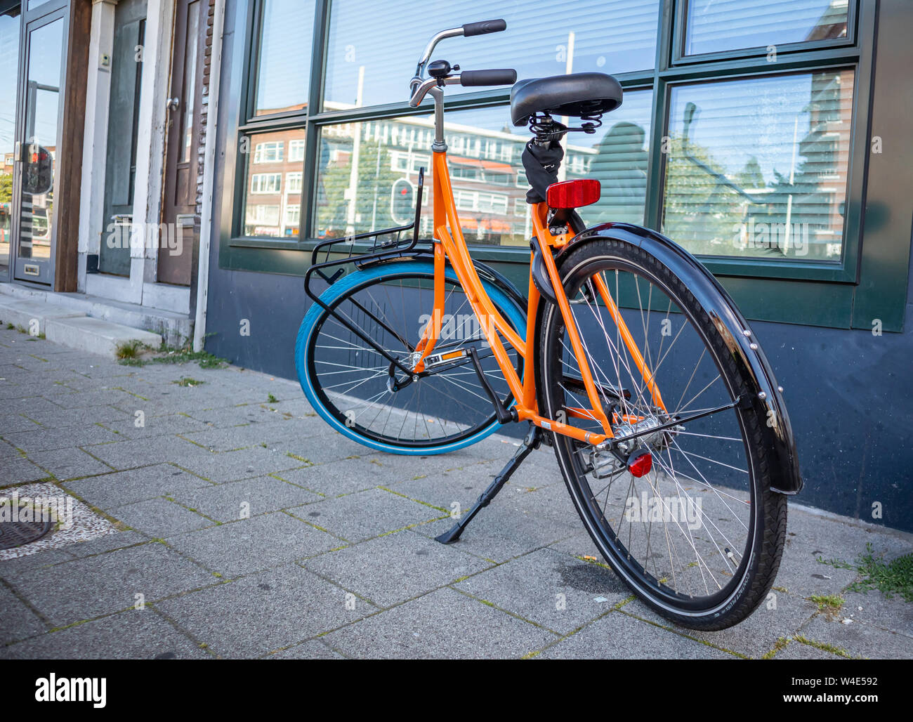 Bike sbloccato di colore arancione parcheggiato su un marciapiede pavimentato in città di Rotterdam, Paesi Bassi. Facciata di edificio sullo sfondo Foto Stock