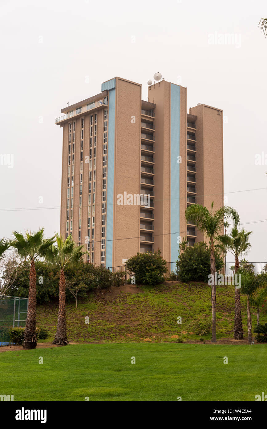 Grattacielo alto edificio di appartamenti in collina con erba verde e le palme sotto cieli grigi. Foto Stock
