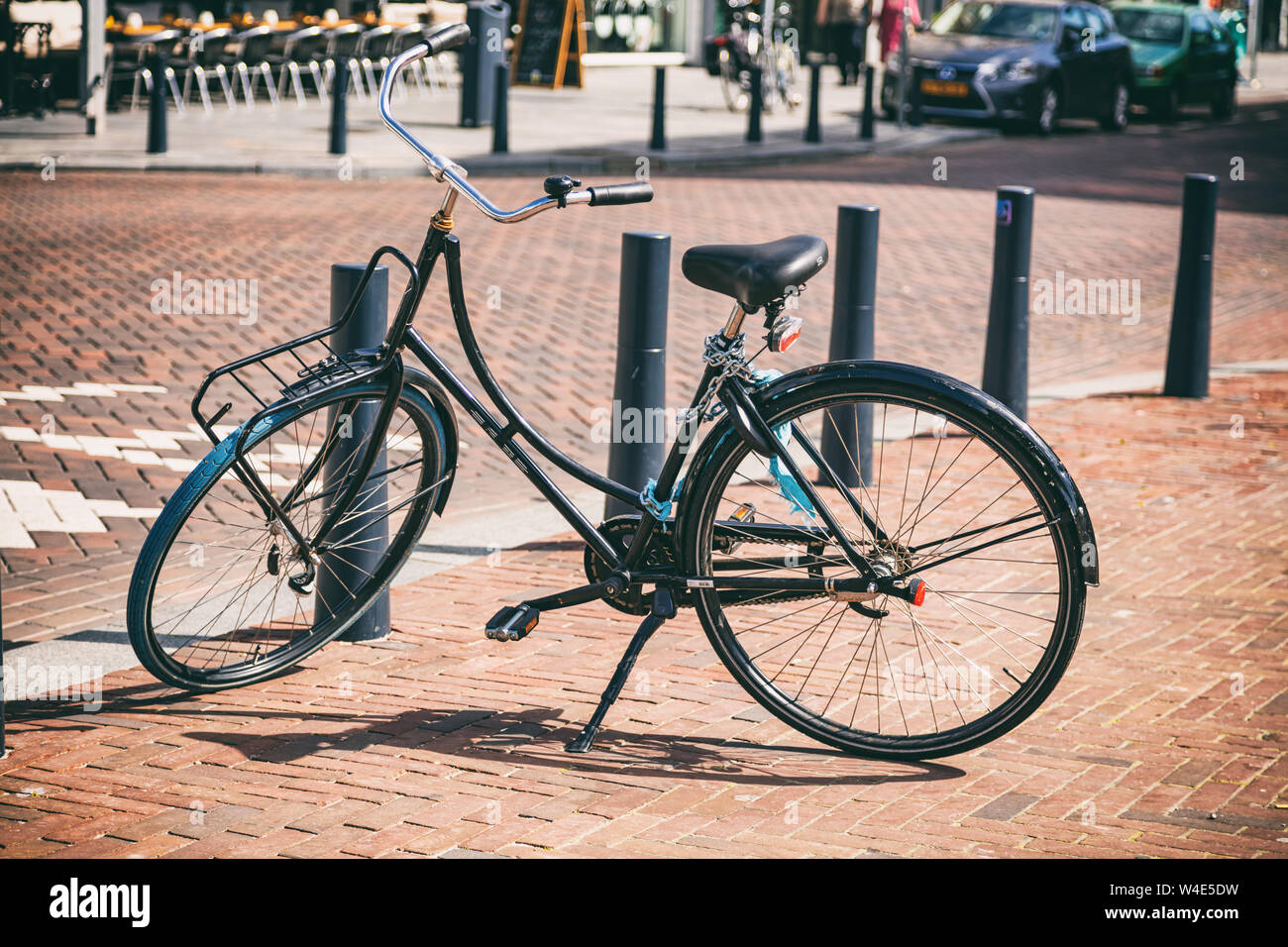Bike sbloccato il colore nero parcheggiato su un marciapiede pavimentato in città di Rotterdam, Paesi Bassi. Blur per le strade delle città sullo sfondo Foto Stock
