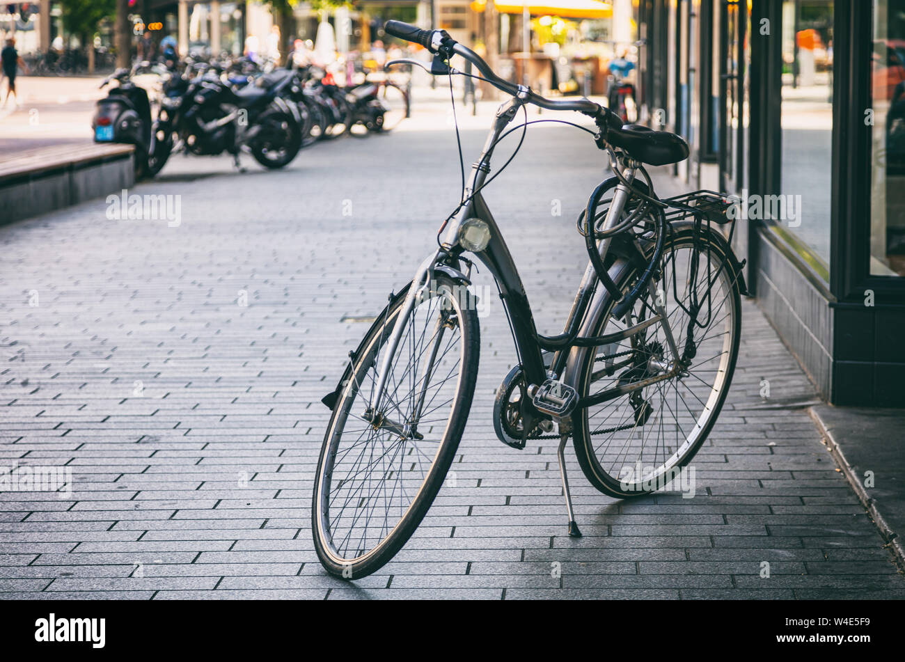Bike sbloccato il colore nero parcheggiato su un marciapiede pavimentato in città di Rotterdam, Paesi Bassi. Blur per le strade delle città sullo sfondo Foto Stock