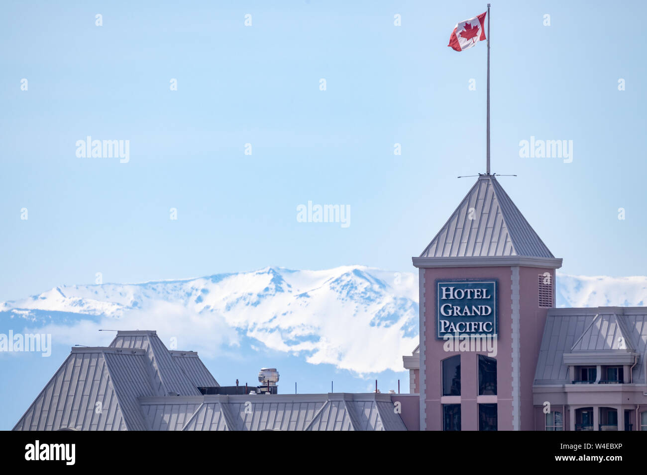 Top of Hotel Grand Pacific con bandiera canadese ondeggiante in una giornata di sole e montagne coperte di neve sullo sfondo. Foto Stock