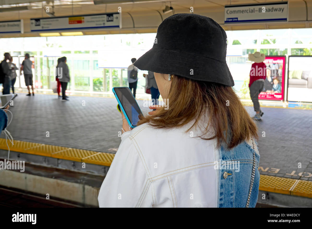 Una giovane donna in dark hat texting sul suo telefono cellulare mentre si è in attesa per un skytrain in Vancouver, B. C., Canada. Foto Stock