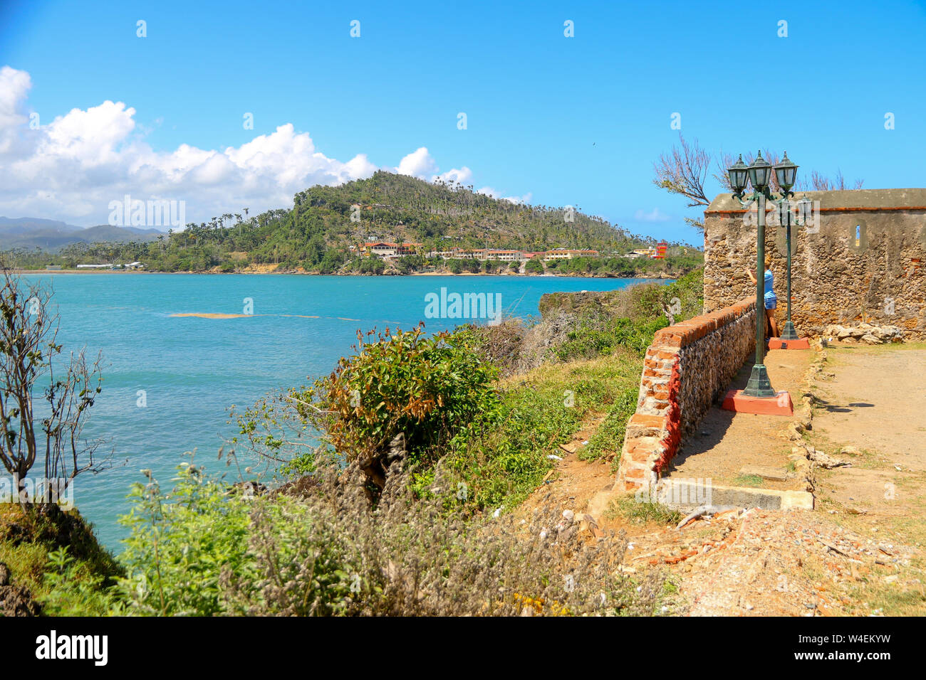 Mar dei Caraibi come si vede in Baracoa, a sud-est di Cuba, con un vecchio muro di mattoni in primo piano. Un'isola verde è visibile in background. Foto Stock