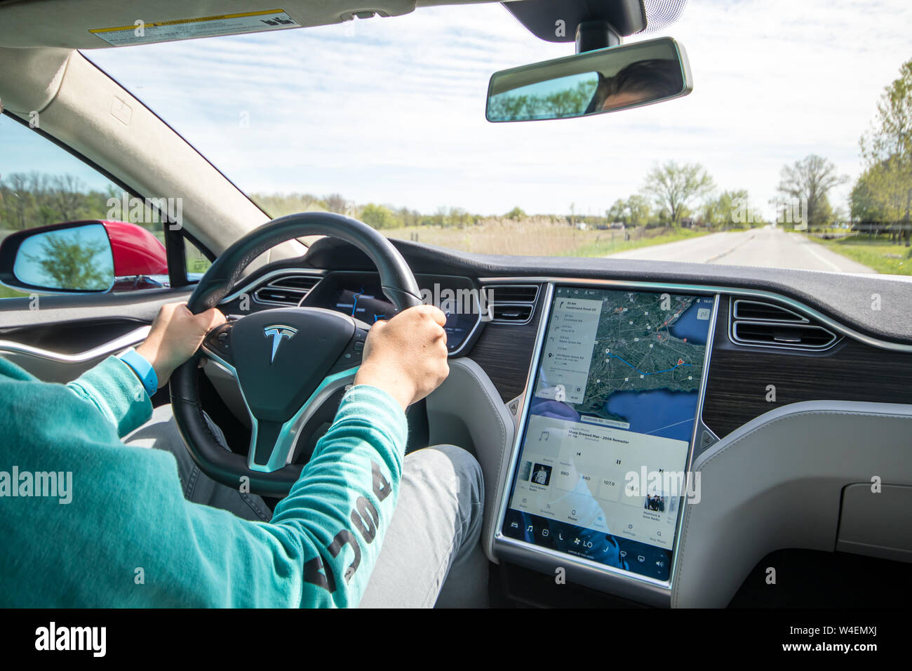 Uomo alla guida di Rosso Modello Tesla S con navigazione sullo schermo accanto. Interno rivestito in bianco e nero e in pelle grigia. Foto Stock