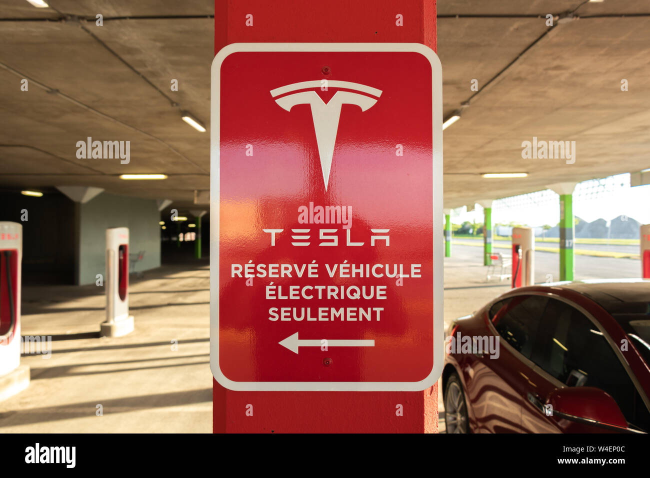 Tesla "Réservé Véhicule Électrique Seulement' (Riservato per Tesla Veicoli Elettrici solo in inglese) segno di Tesla Supercharger, Rosso Modello S accanto a. Foto Stock