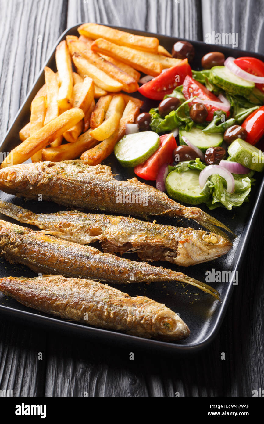 Fried Boops boops pesce con un contorno di insalata fresca e patatine fritte close-up su una piastra sul piano verticale. Foto Stock
