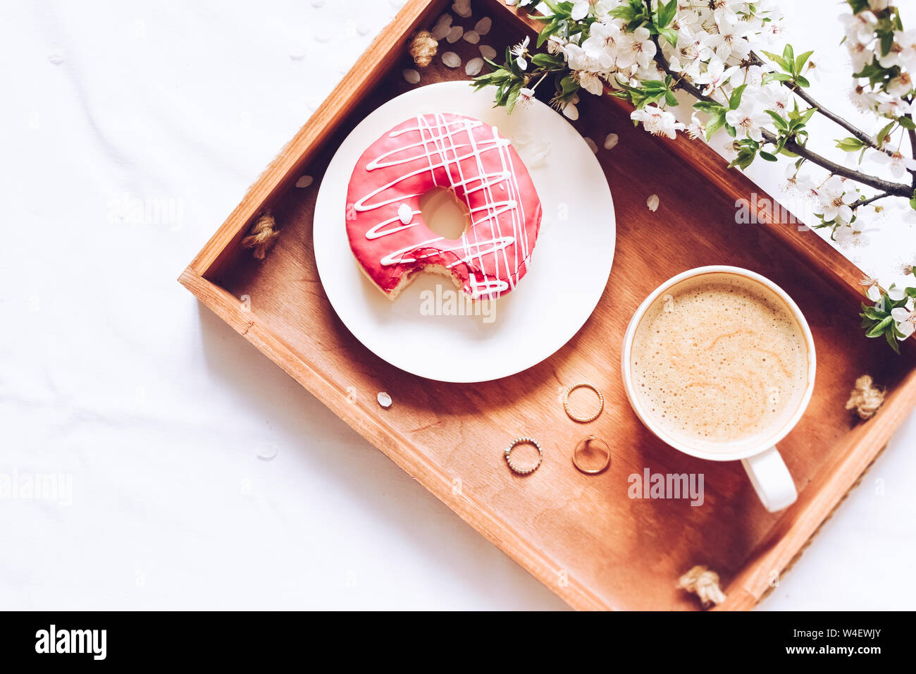 La molla brealfast nel letto. Vassoio con Fragola Rosa ciambella con caffè e la primavera sbocciano i fiori. Ragazza la lettura di un libro. Vista dall'alto. Copia dello spazio. Foto Stock