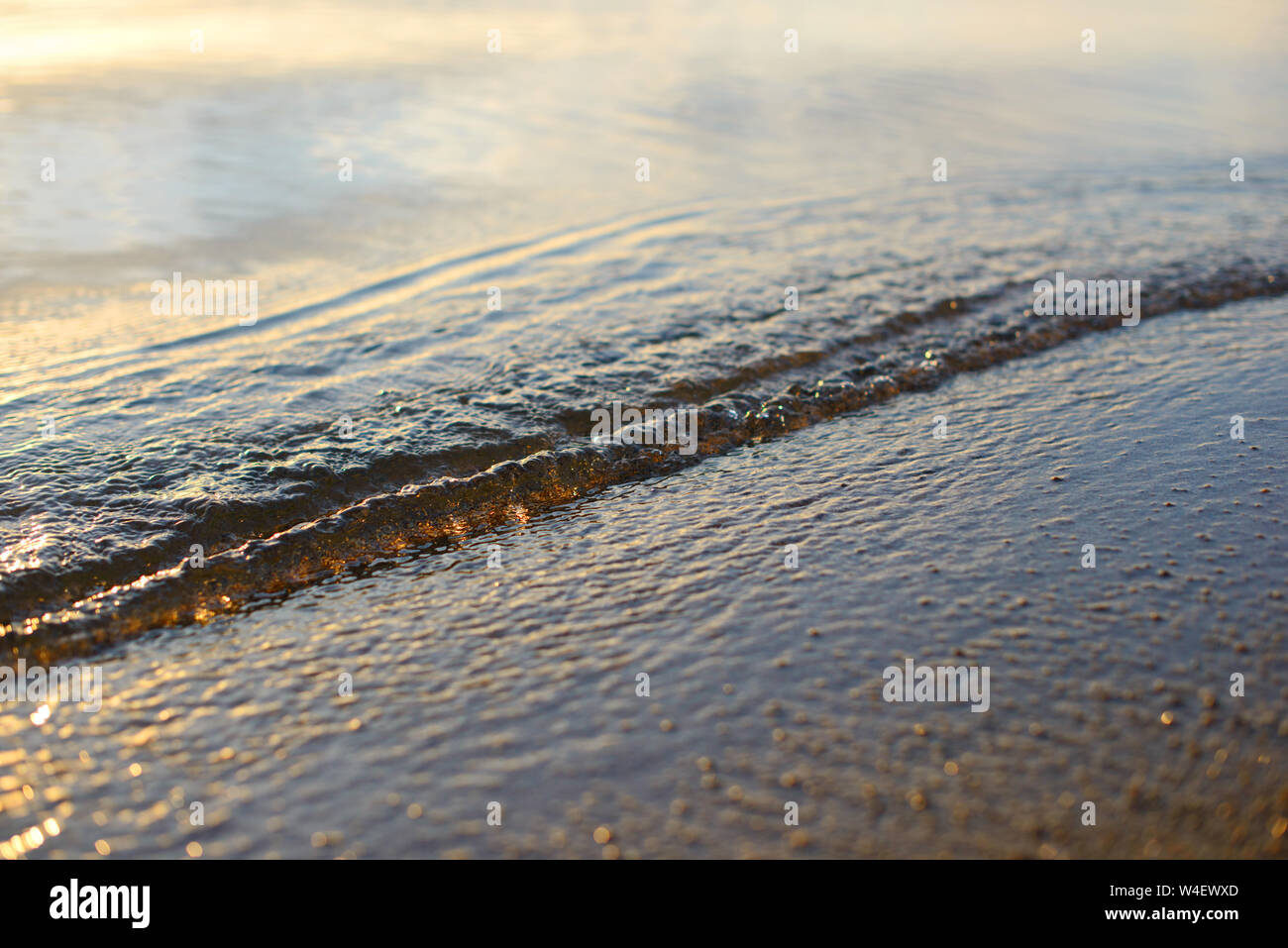 Onda di mare e spiaggia di sabbia. Golden Sun luce oltre il mare oceano onde. Riflessione speculare sulla superficie dell'acqua. Macro close up. Foto Stock