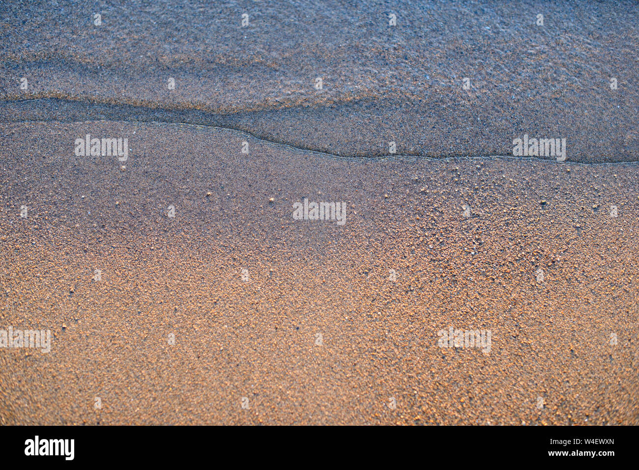 Onda di mare e spiaggia di sabbia. Golden Sun luce oltre il mare oceano onde. Riflessione speculare sulla superficie dell'acqua. Macro close up. Foto Stock