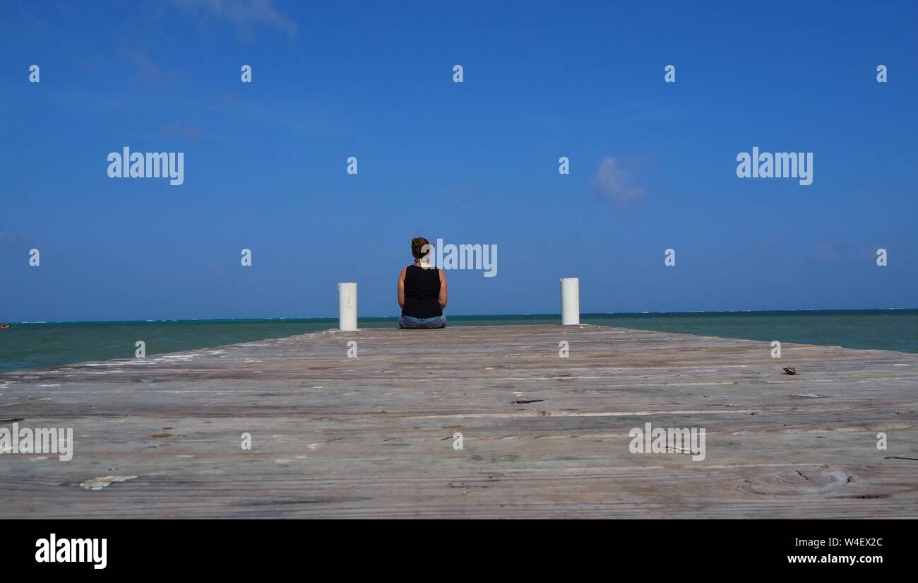 Ragazza seduta su un molo che guarda al mare. Femmina singolo viaggiatore solitario. Foto Stock