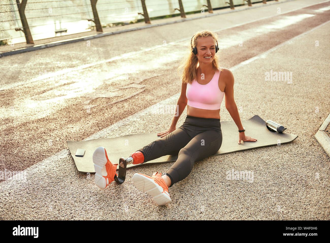 Sport con la musica. Disabili positivo atleta donna con gamba protesico in ascolto in cuffia musica e sorridere mentre esercita sul ponte. Sport disabili concetto. La motivazione. Uno stile di vita sano Foto Stock