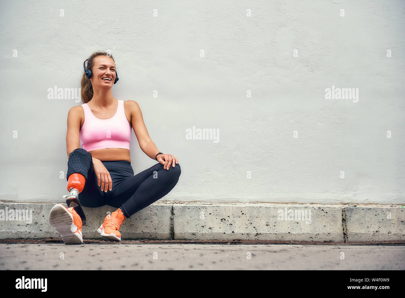Semplicemente felice giovane donna sorridente con protesi di gamba in  abbigliamento sportivo e di ascolto in cuffia la musica dopo il suo  allenamento mentre seduti all'aperto. Sport disabili concetto. La  motivazione. Musica