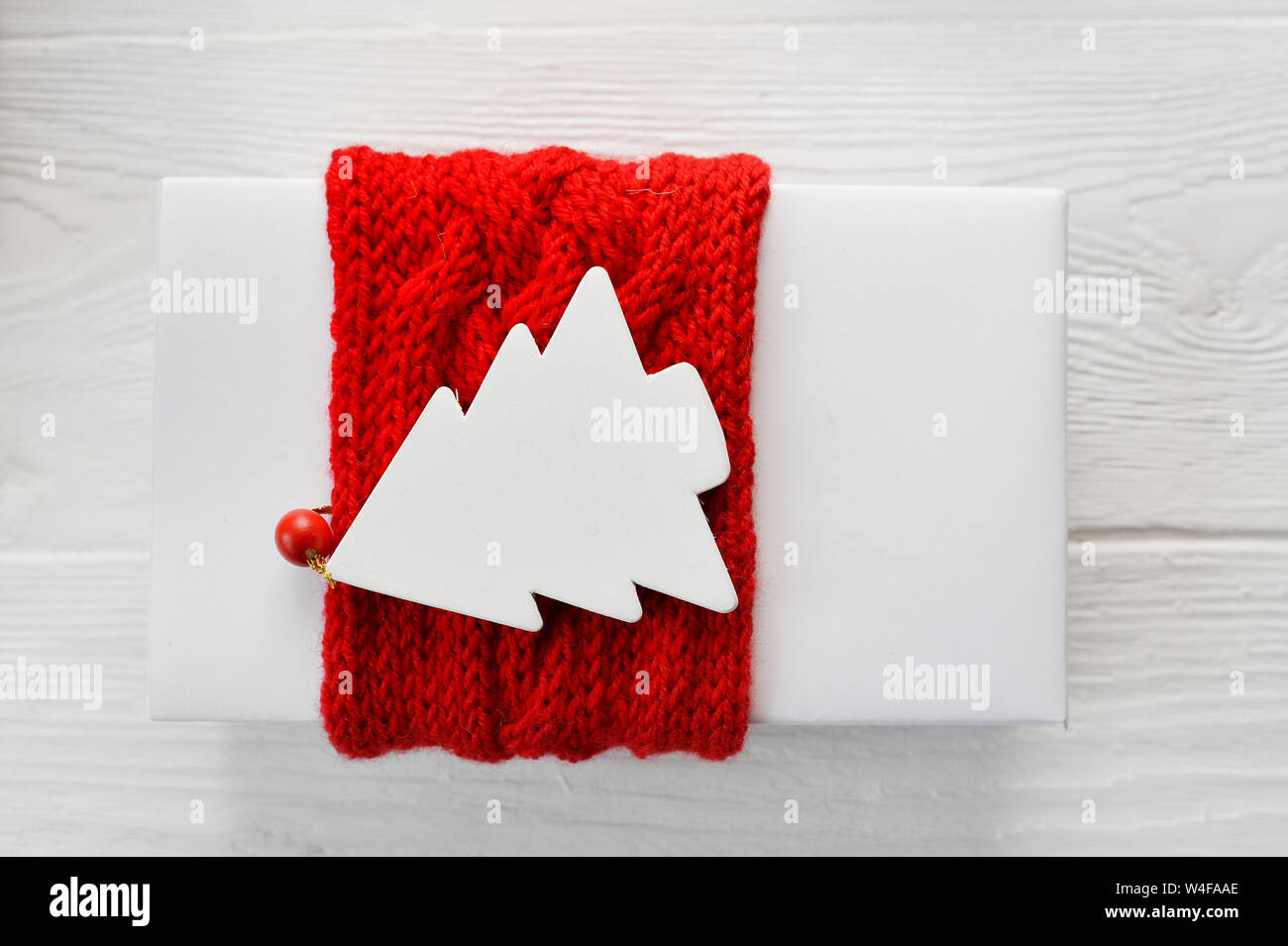 White Christmas Gift Box ROSSO con nastro a maglia e mockup tag nella forma di abete su sfondo bianco. Close up vista superiore Foto Stock