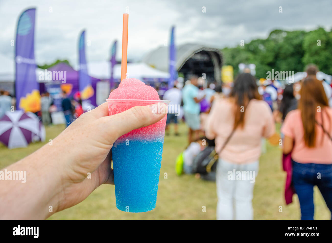 Un maschio di mano che tiene un slushie bere in un campo in un festival. Un slushie è una bevanda fatta dal ghiaccio aromatizzato. Foto Stock