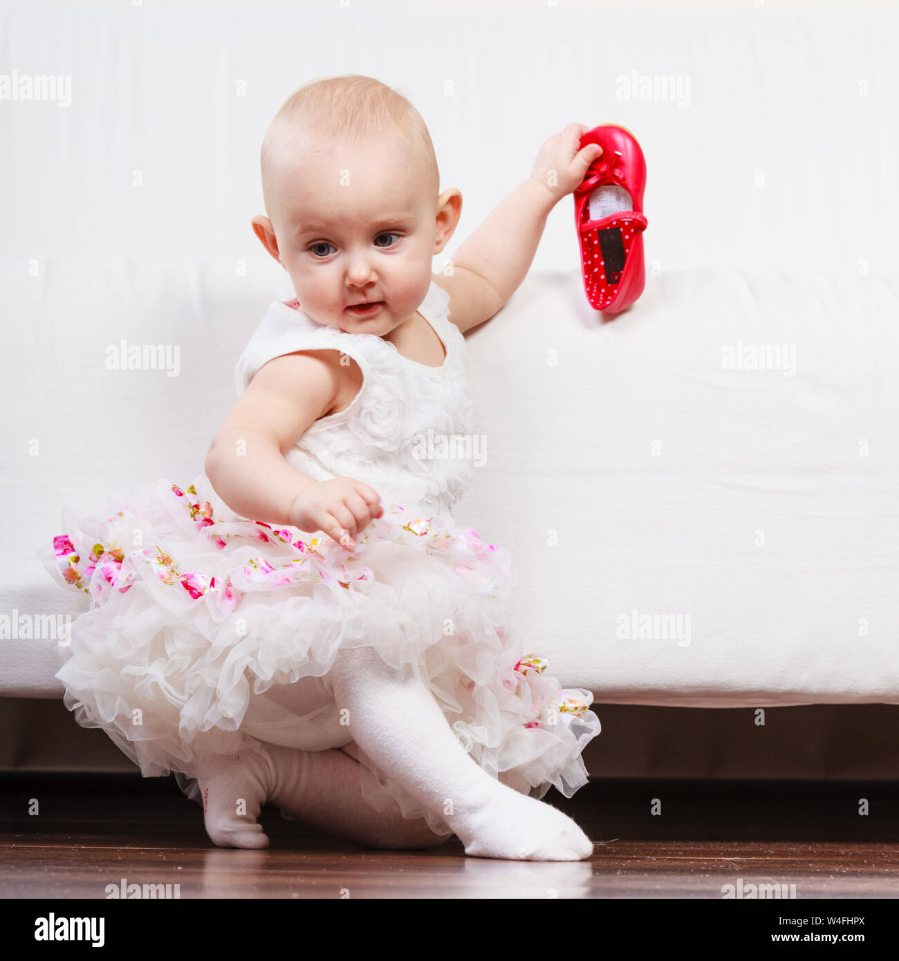 Lezione di camminata. Dolce adorabile bambina facendo passi a casa. Bambino toddler indossando la principessa abito rosso con piccole scarpe. Foto Stock