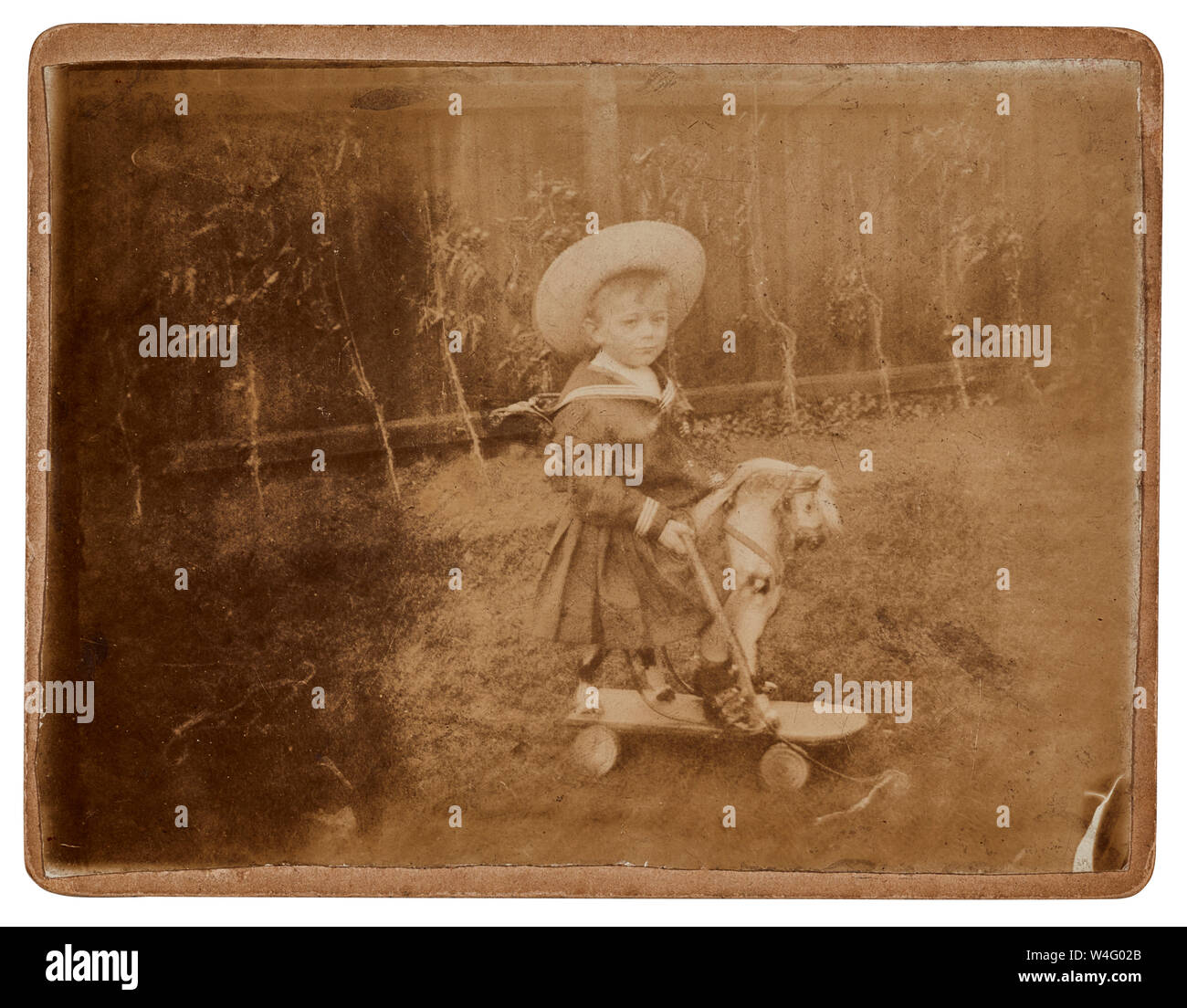 Ragazzo seduto su un cavallo giocattolo vestito con una tuta marinaio e indossando un cappello da un Edwardian fotografia Foto Stock
