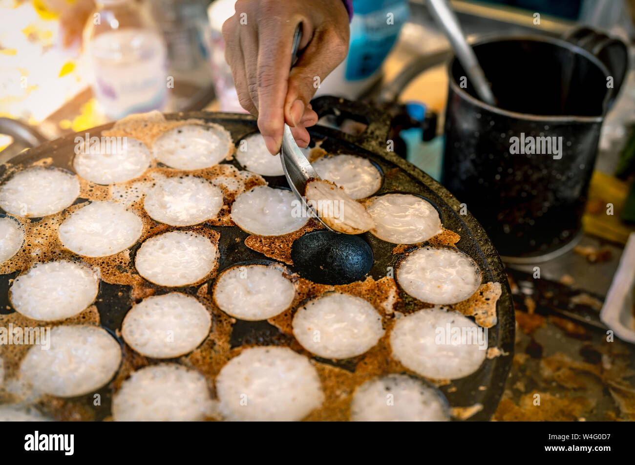 Malta-pasticceria tostato o 'Kanom Krok' è Thai dessert tradizionale. Donna mano rimozione Kanom Krok da stufa dal cucchiaio. Cucina di strada in Thailandia. Thai Foto Stock