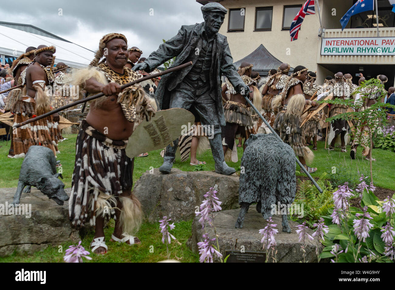 Zulu warriors accanto al drover della statua presso il Royal Welsh showground in Llanelwedd. Visita del re la buona volontà della Nazione Zulu al Royal Welsh Show (RWA) a Builth Wells. Llanelwedd, POWYS, GALLES. Foto Stock