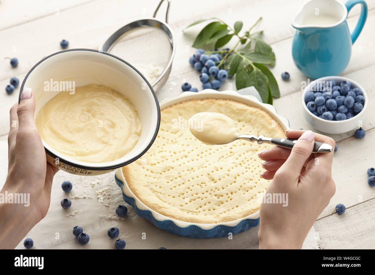 Donna versando la panna montata sulla base di pastafrolla. Torta ai mirtilli o crostata ricetta di cucina. Foto Stock