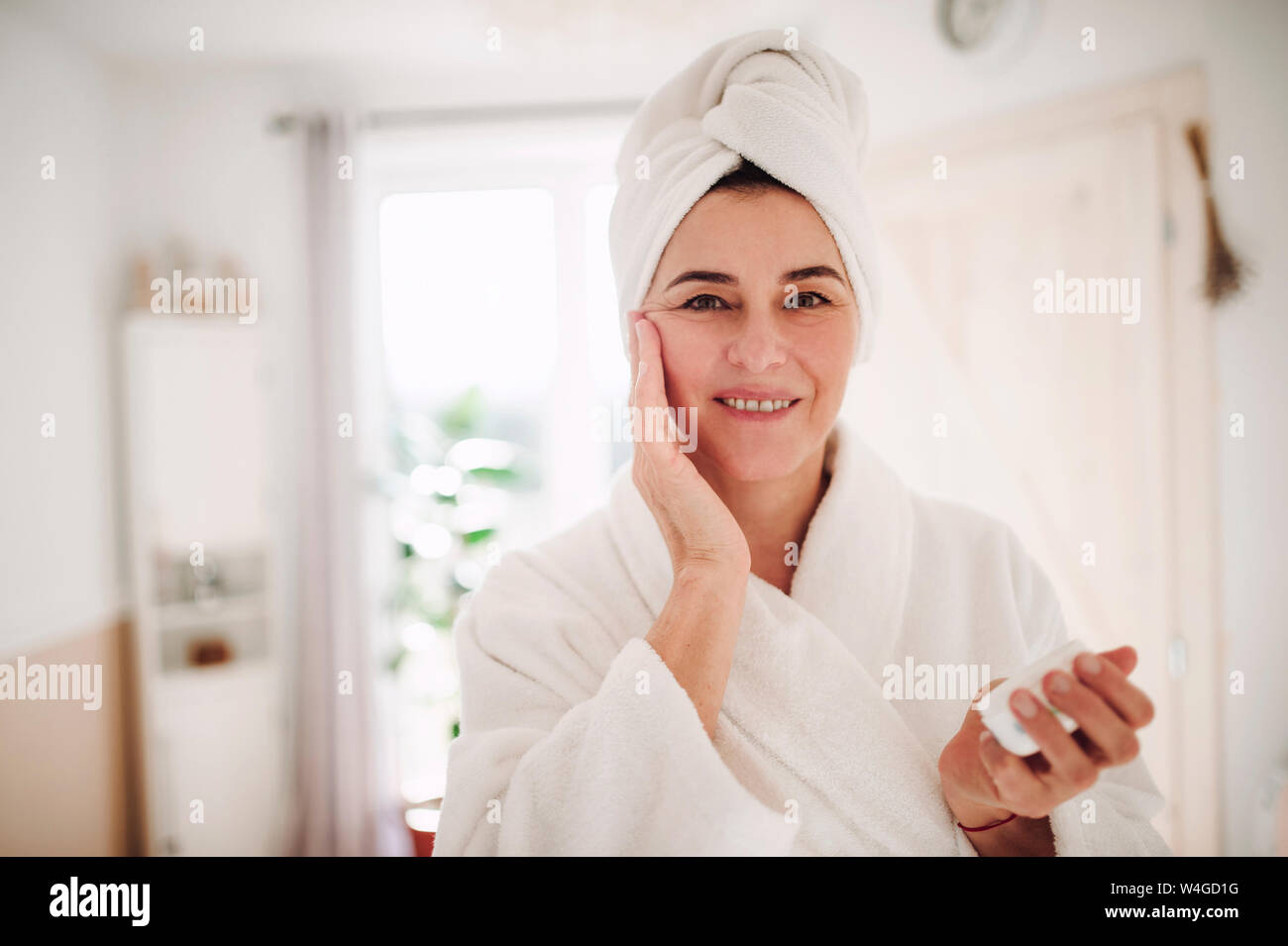 Ritratto di donna matura in un bagno a casa di applicare una crema idratante Foto Stock