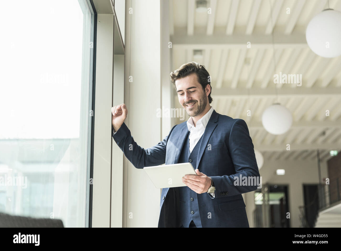 Manager di successo in piedi in un ufficio moderno edificio, utilizzando laptop Foto Stock
