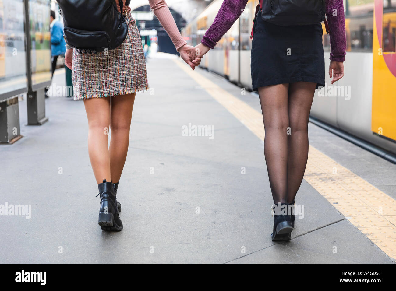 Vista posteriore di due donne con zaini camminando mano nella mano sulla piattaforma, Porto, Portogallo Foto Stock
