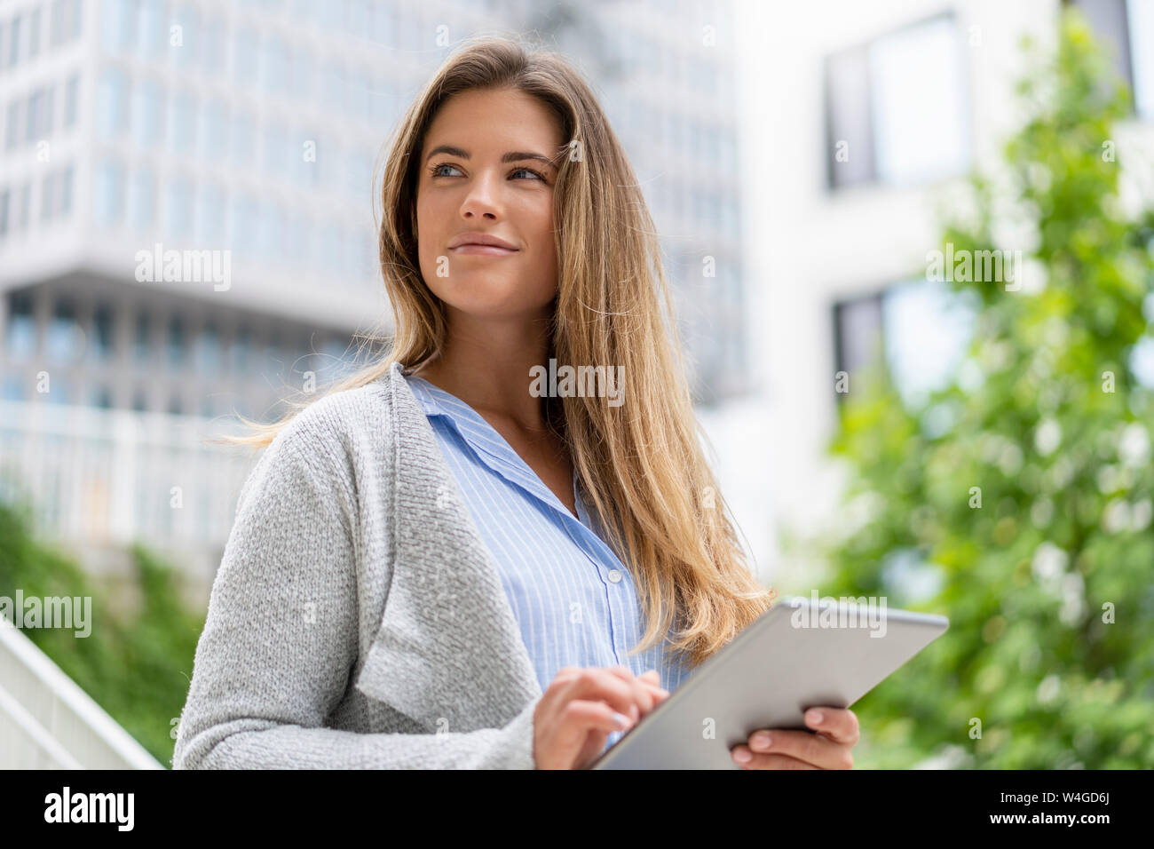 Ritratto di giovane imprenditrice utilizzando tablet, edifici per uffici in background Foto Stock