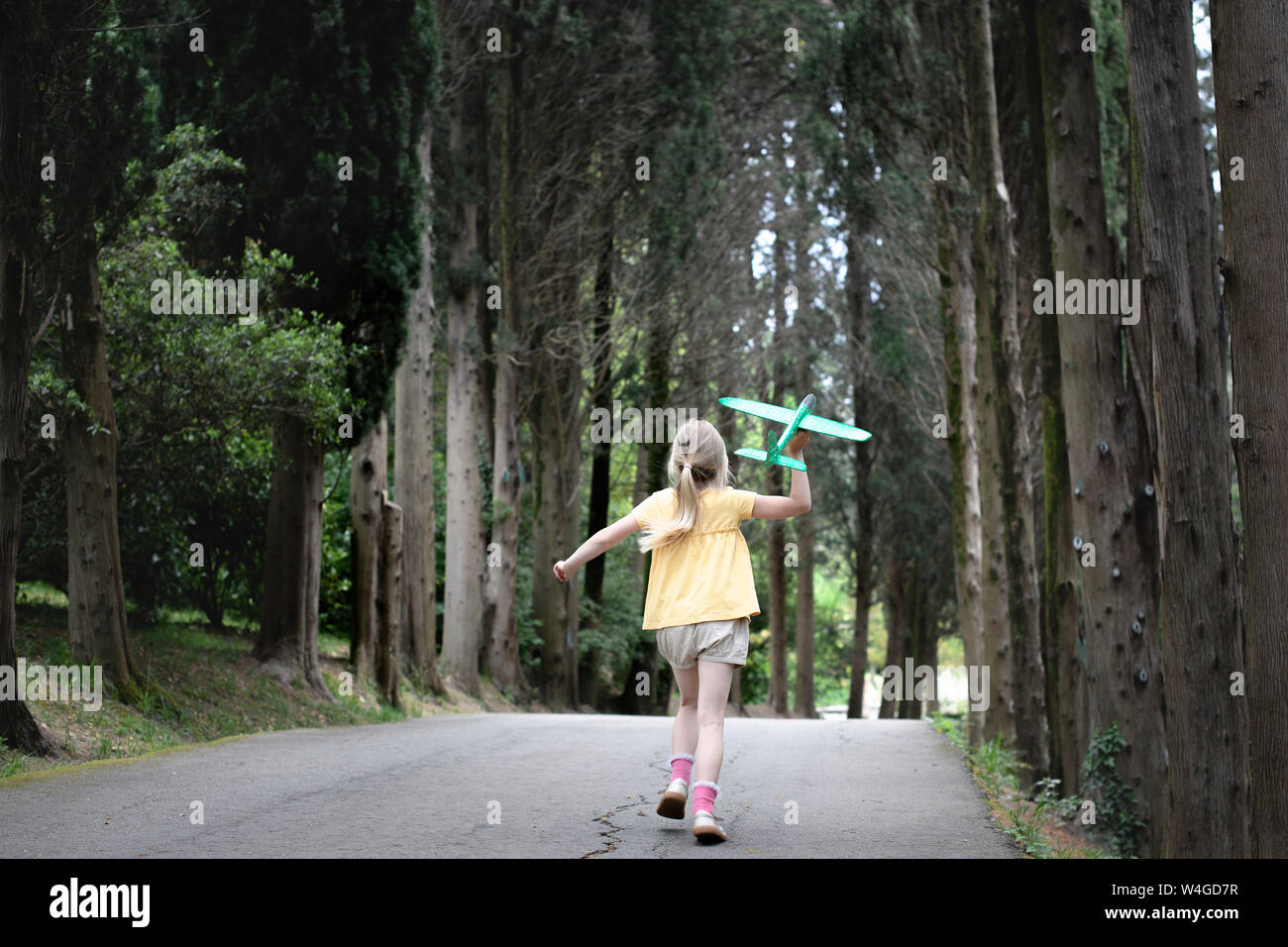 Ragazza con piano giocattolo in esecuzione su una strada orlate da alberi Foto Stock