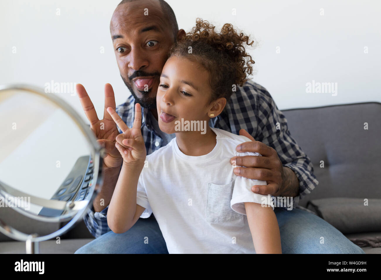 Padre e figlia a casa tirando facce buffe e cercando in specchio Foto Stock