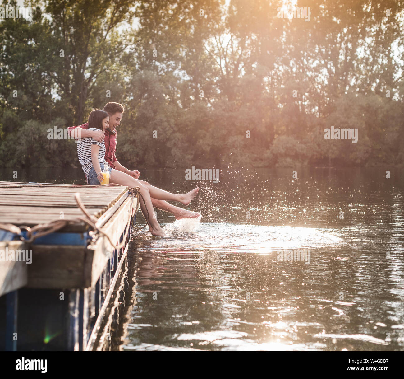 Felice coppia giovane avente un drink e spruzzi con acqua sul pontile di un lago in remoto Foto Stock