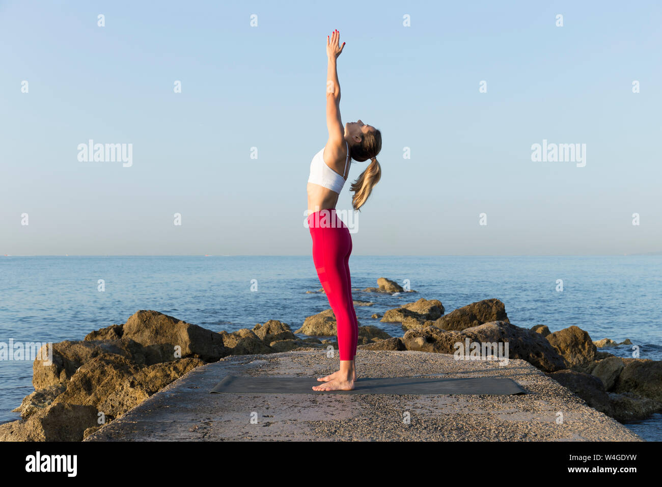 Giovane donna a praticare yoga sulla spiaggia, facendo sun salutations Foto Stock
