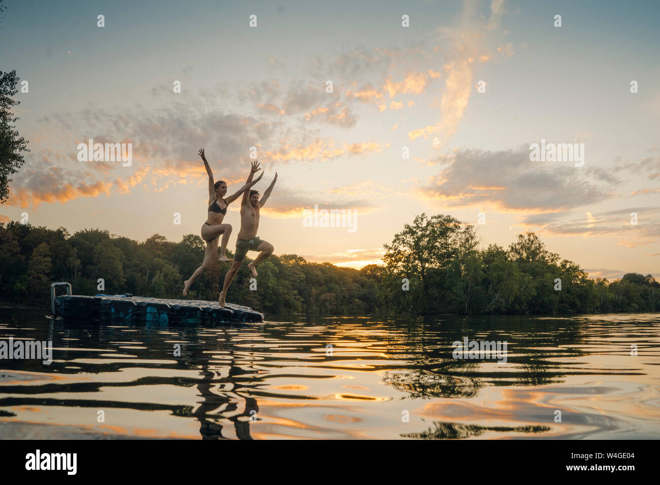 Coppia giovane saltando dalla piattaforma di balneazione sul lago, tenendo le mani Foto Stock