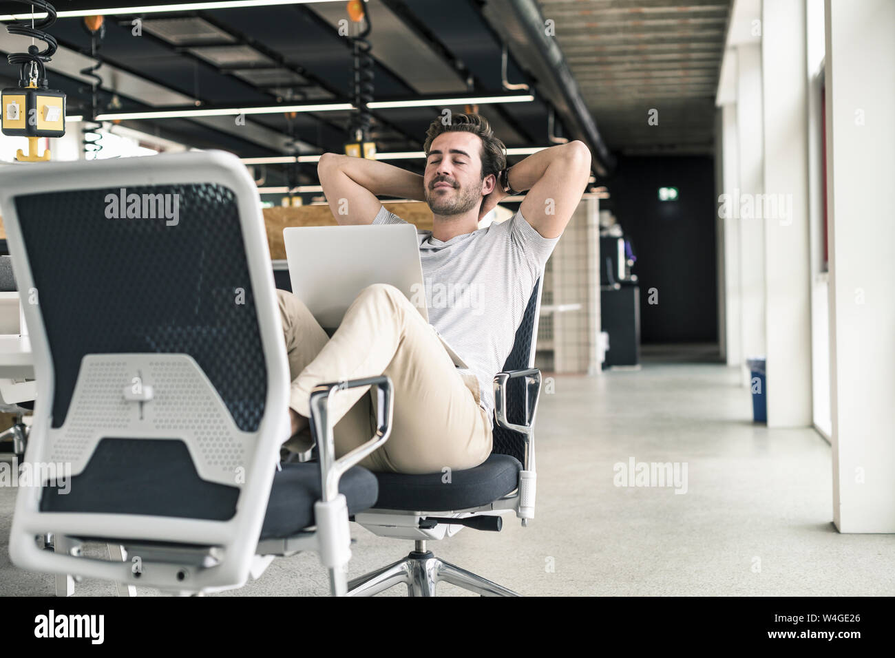 Giovane imprenditore lavora rilassato in un ufficio moderno, con laptop in giro Foto Stock