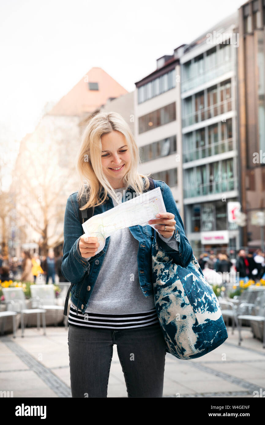 Ritratto di sorridere donna bionda bagaglio guardando la mappa della città di Monaco di Baviera, Germania Foto Stock