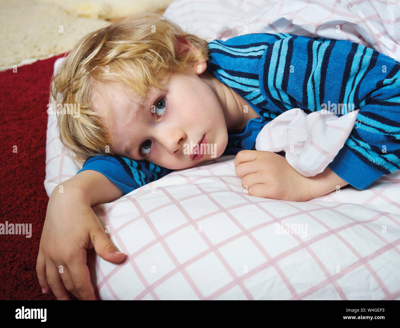 Ritratto di Little Boy sdraiato sul pavimento con biancheria da letto Foto Stock