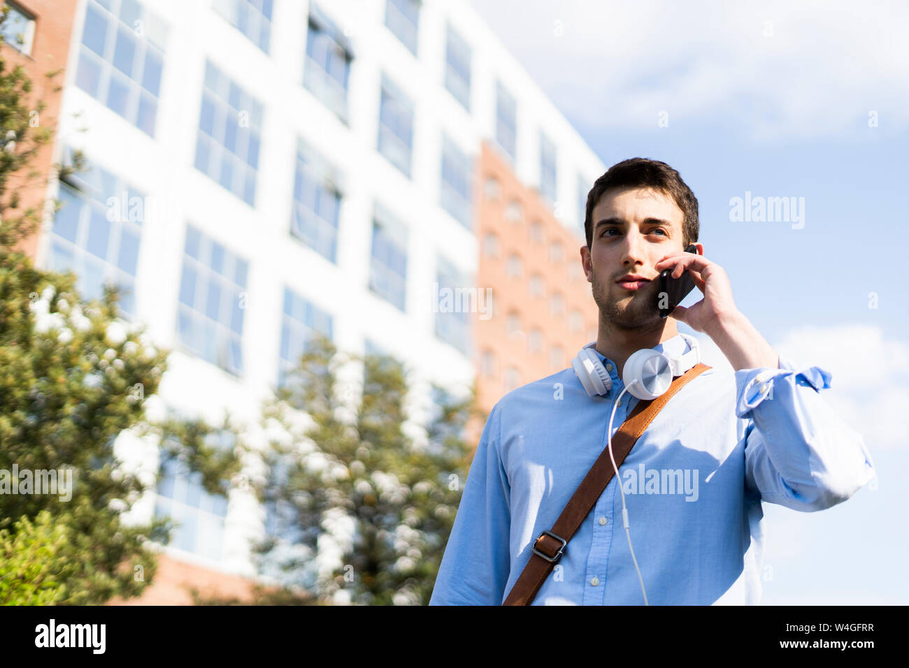 Giovane uomo utilizza lo smartphone, cuffie attorno al collo in città Foto Stock