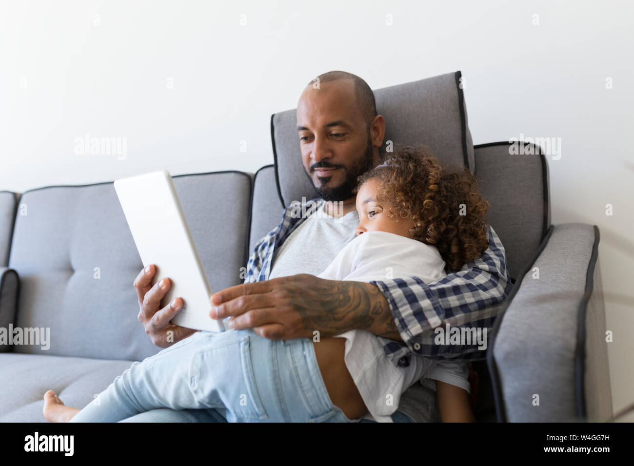 Padre e figlia seduti sul divano di casa insieme guardando tablet Foto Stock