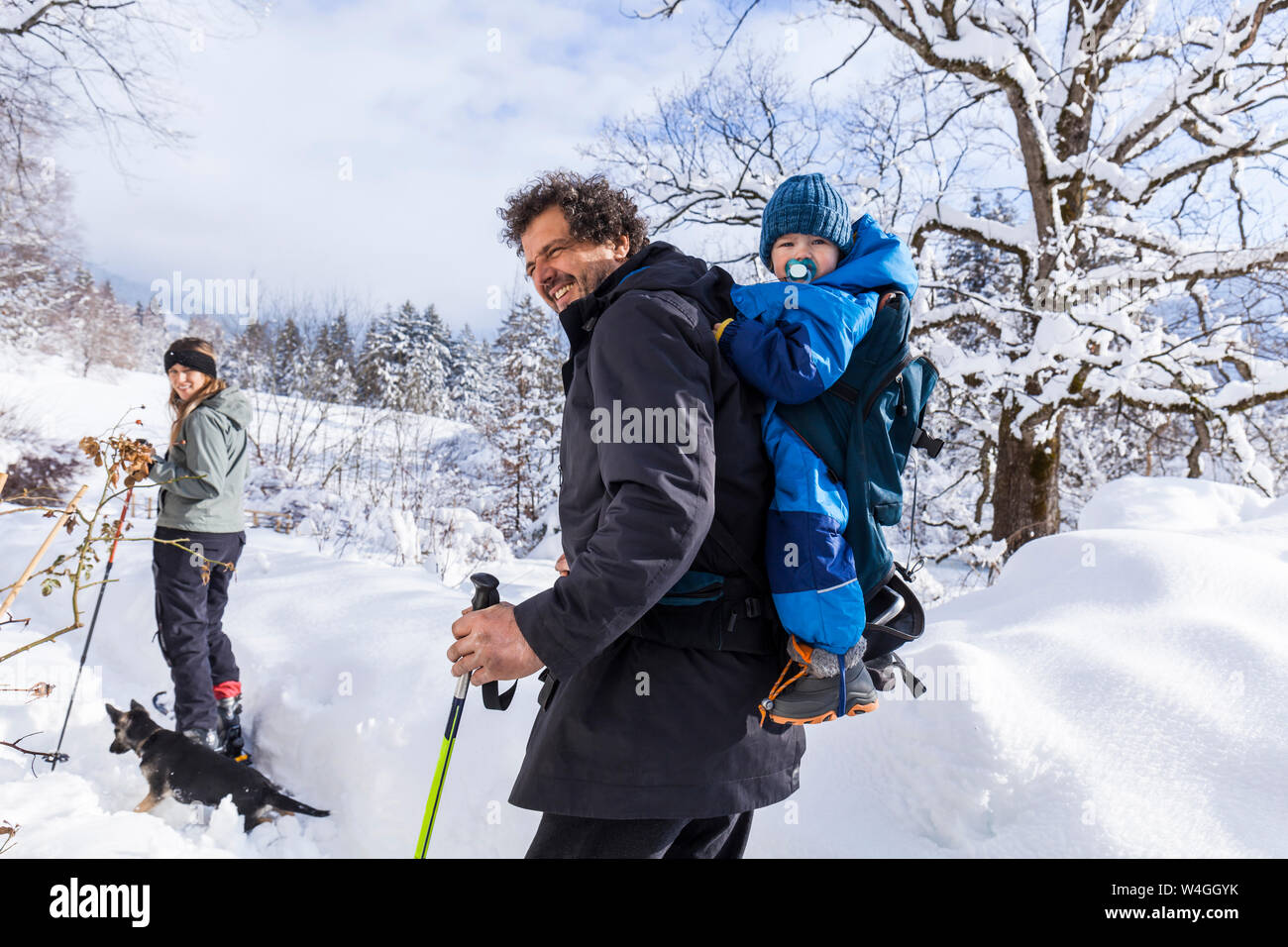 Padre con il figlio nel bambino portatore, madre e cane in Oberammergau in inverno Foto Stock
