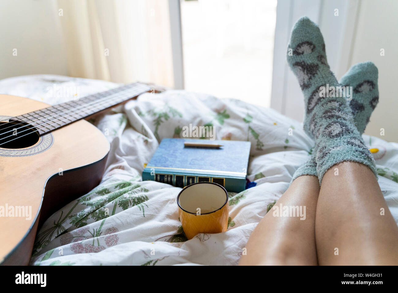 Donna sdraiata sul letto con la chitarra, il libro e la tazza di caffè, vista parziale Foto Stock