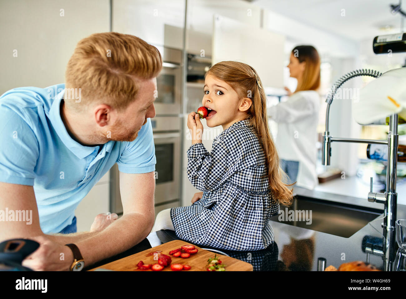 La famiglia felice di mangiare fragole fresche in cucina moderna Foto Stock