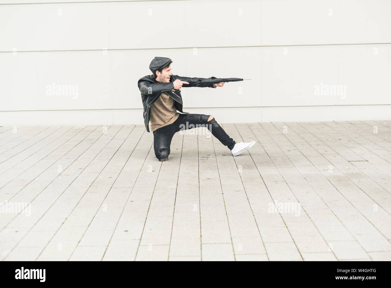 Giovane uomo fingendo di sparare con ombrello chiuso Foto Stock