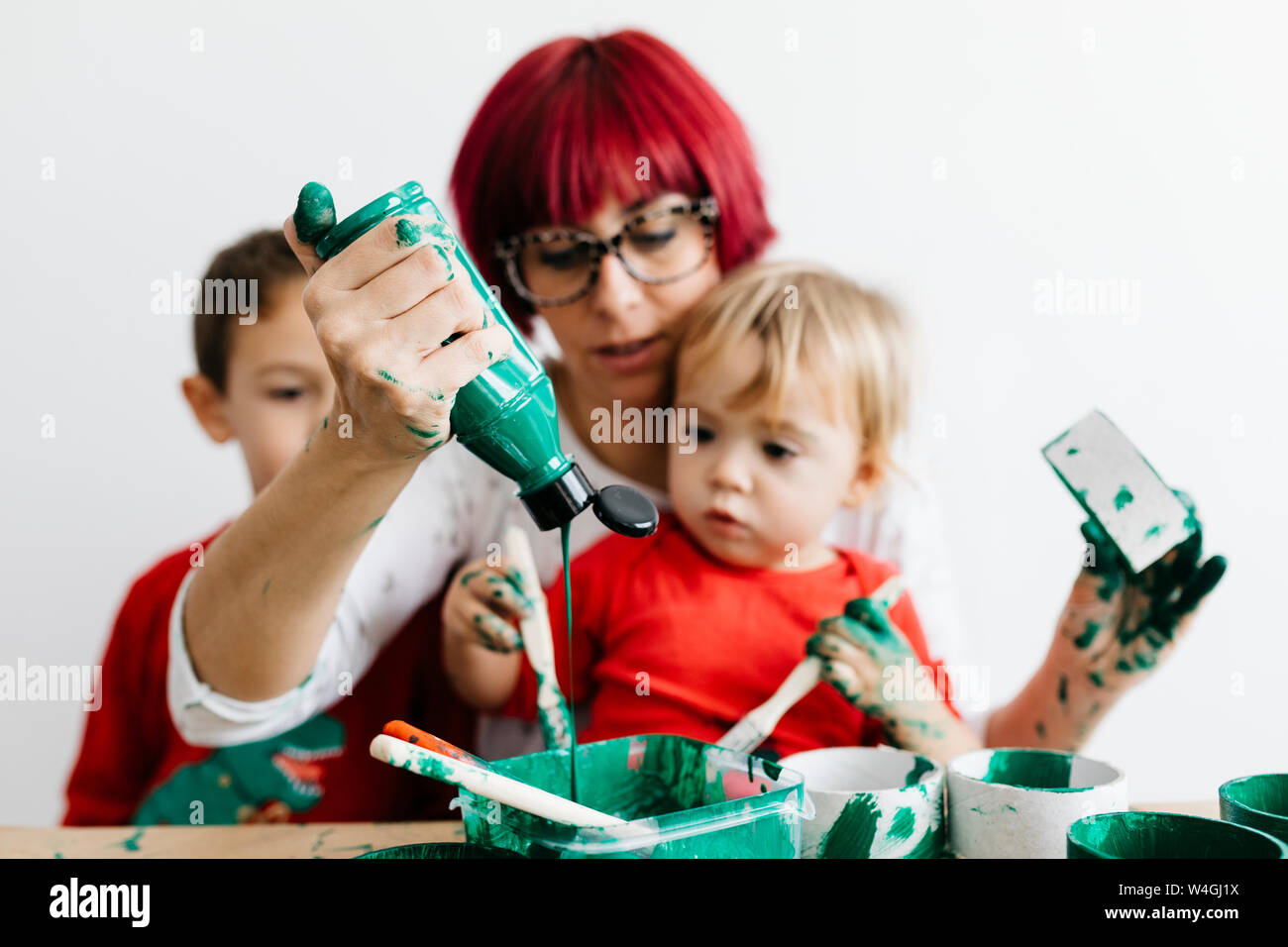 Madre con i suoi figli fare artigianato a casa e dipingere con il verde Foto Stock