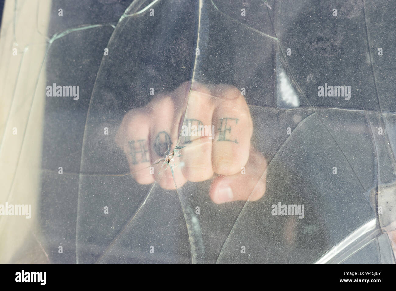 Pugno di un giovane uomo di speranza tatuaggio dietro il parabrezza rotto su un scrapyard Foto Stock