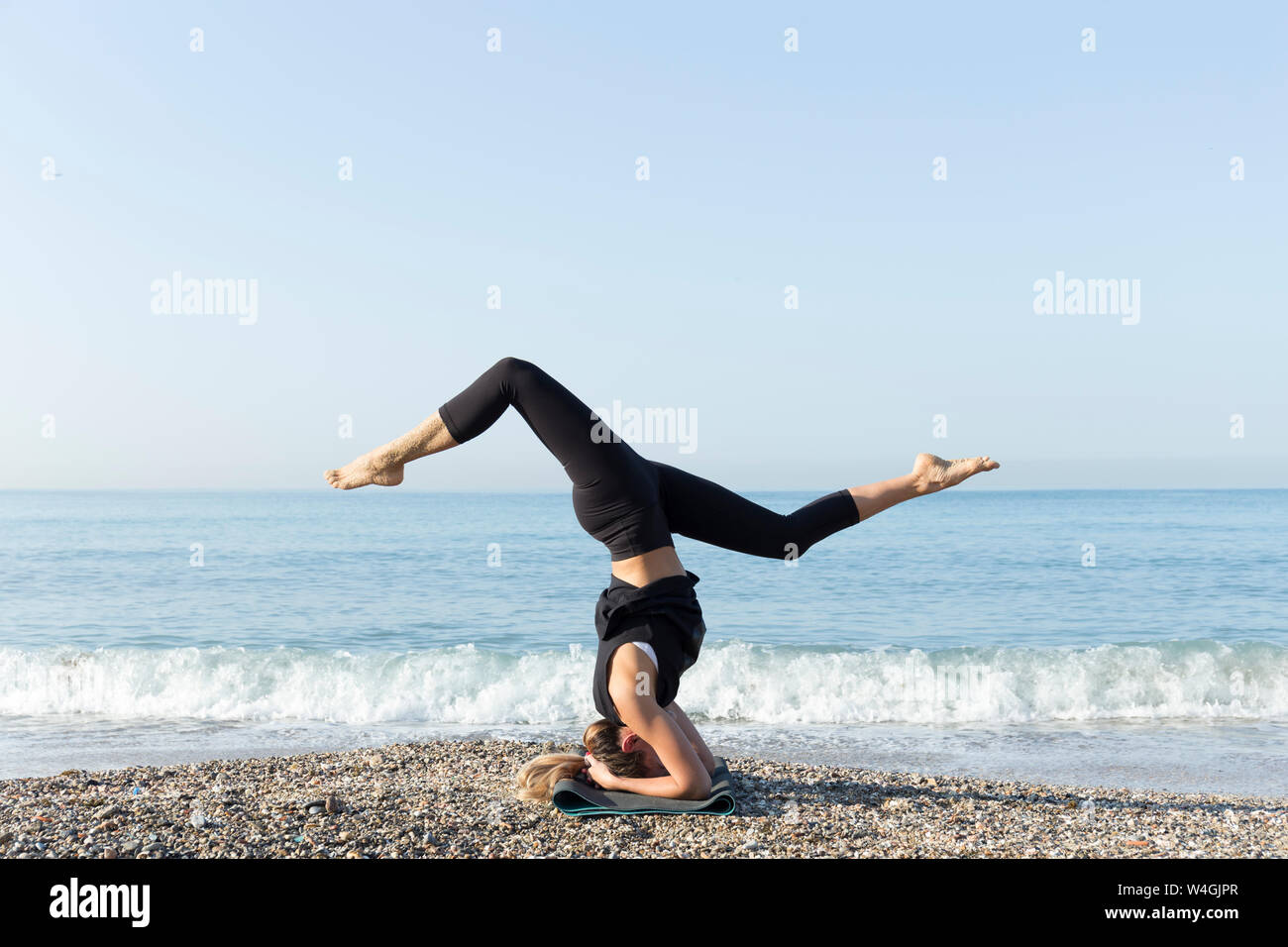 Giovane donna a praticare yoga sulla spiaggia, facendo headstand Foto Stock