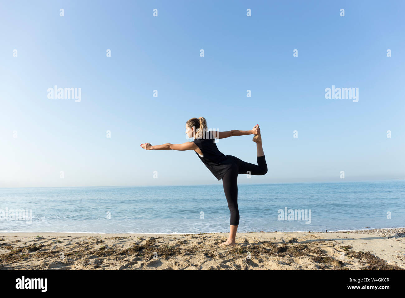 Giovane donna a praticare yoga sulla spiaggia, facendo la posizione del signore della danza Foto Stock